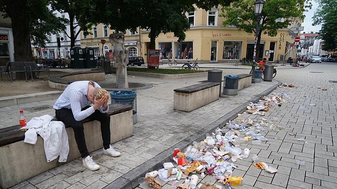 Student Leo nach einer durchgemachten Nacht sitzt er morgens um 6.30 Uhr am Wedekindplatz auf einer Bank. Auf der Straße türmt sich der Abfall.