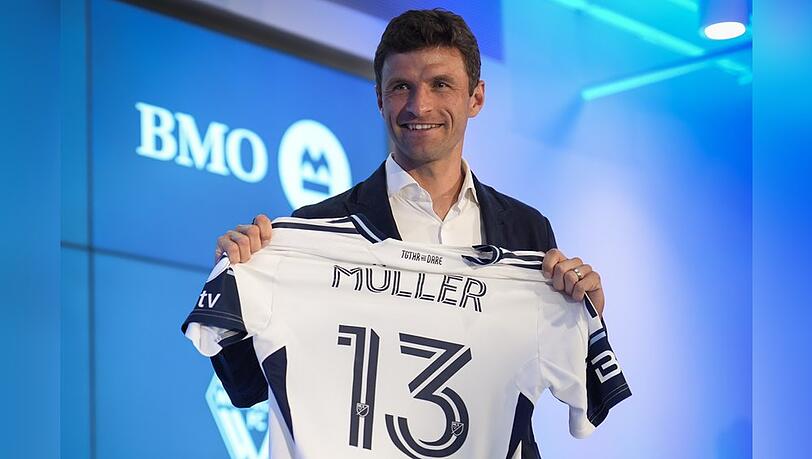 Stolz zeigt Thomas Müller bei einer Pressekonferenz in Vancouver sein Trikot, das ebenfalls seine legendäre Nummer 13 trägt.