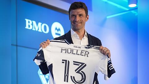 Stolz zeigt Thomas Müller bei einer Pressekonferenz in Vancouver sein Trikot, das ebenfalls seine legendäre Nummer 13 trägt.