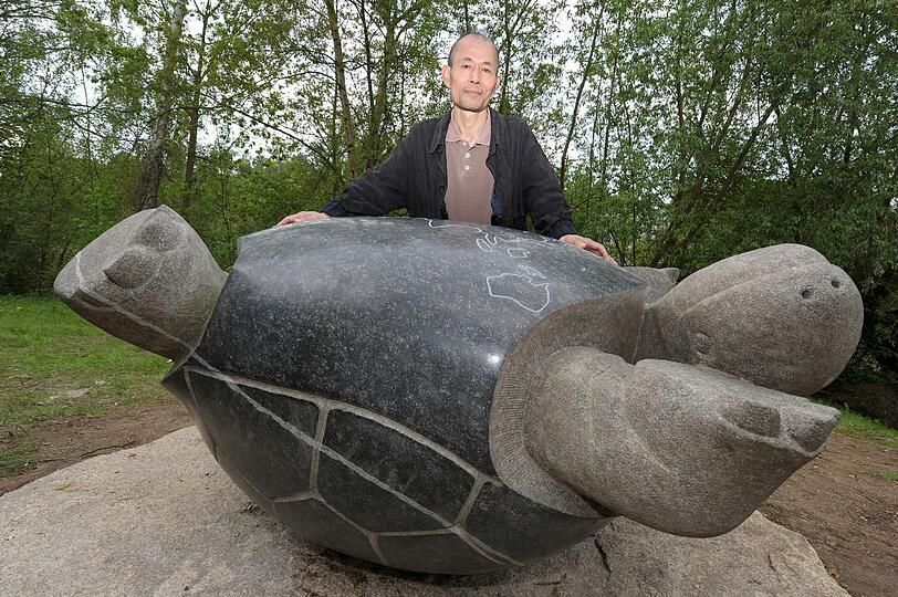 Der koreanische  Bildhauer Jin Mo Kang kniet am Dienstag in Bamberg hinter seinem Tschernobyl-Denkmal, einer auf dem Rücken liegenden Schildkröte.