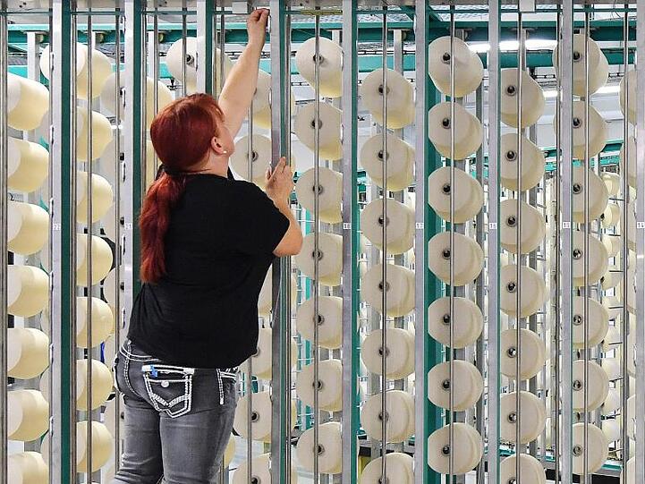 Eine Mitarbeiterin bestückt in der Getzner Textilweberei GmbH die sogenannte Zettelmaschine mit Garn. Foto: Martin Schutt/Archiv