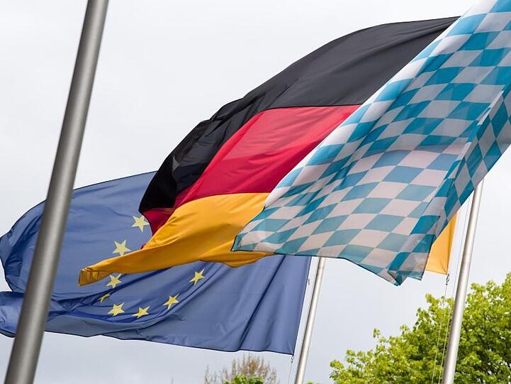 Die Europa-, Deutschland- und Bayernfahne wehen nebeneinander im Wind. Foto: Peter Kneffel/Archivbild