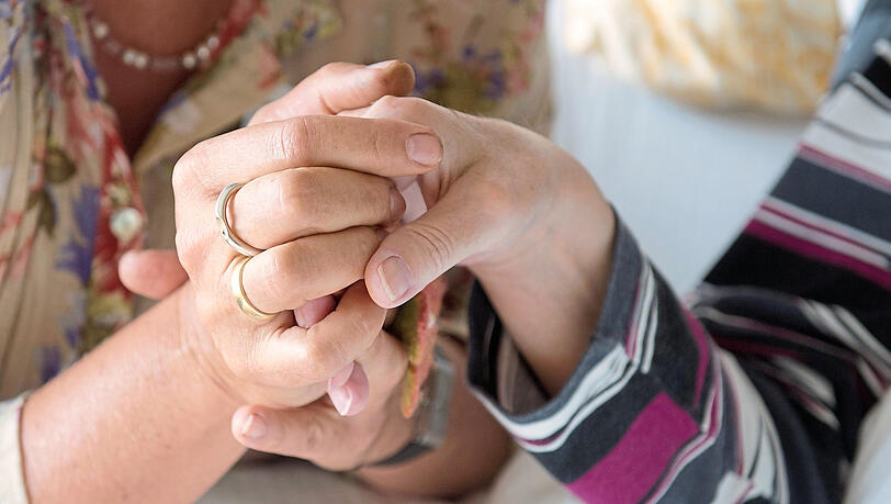 Eine Therapeutin in einem Hospiz hält die Hand einer todkranken Bewohnerin.