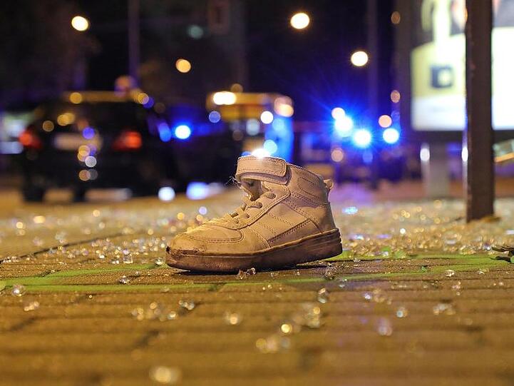Ein Sportschuh liegt nach dem Verkehrsunfall an einer Bushaltestelle zwischen Glasscherben.