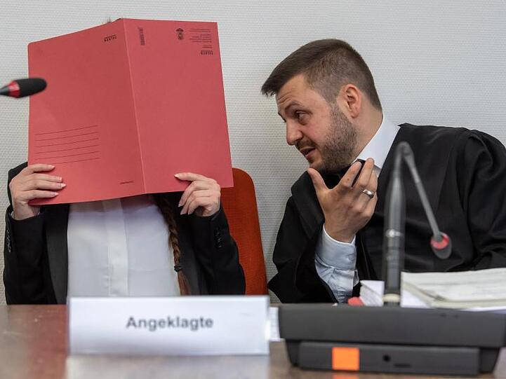 Die Angeklagte hält auf ihrem Sitz im Gerichtssaals einen roten Aktendeckel vor ihr Gesicht. Rechts spricht ihr Anwalt Ali Aydin mit ihr. Foto: Peter Kneffel/dpa/Archiv