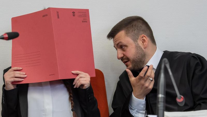 Die Angeklagte hält auf ihrem Sitz im Gerichtssaals einen roten Aktendeckel vor ihr Gesicht. Rechts spricht ihr Anwalt Ali Aydin mit ihr. Foto: Peter Kneffel/dpa/Archiv
