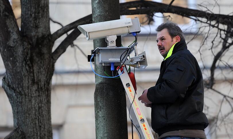 Ein Mann macht vor dem Bayerischen Hof eine Überwachungskamera an einem Baum fest.