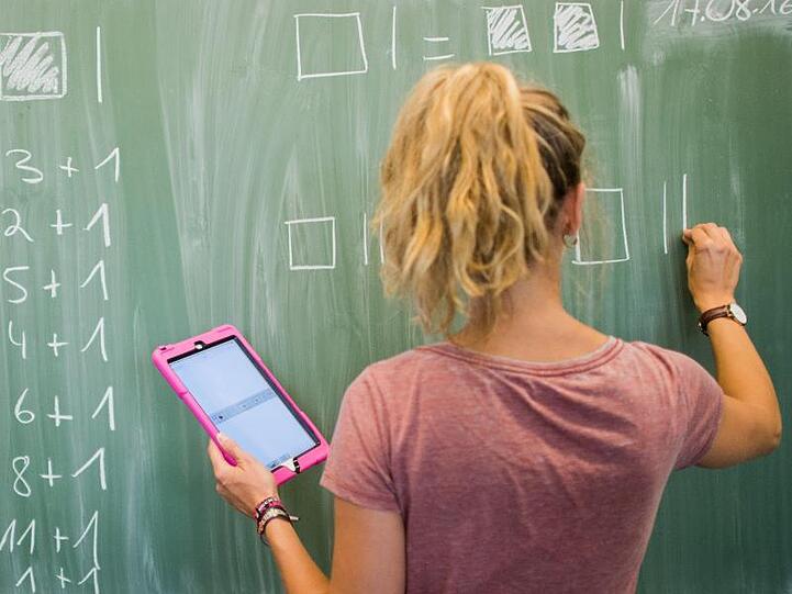 Eine Lehrerin mit Kreide und Tablet im Mathematikunterricht einer 8. Klasse.
