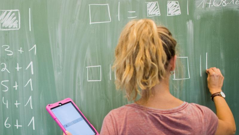 Eine Lehrerin mit Kreide und Tablet im Mathematikunterricht einer 8. Klasse. Eine Lehrerin mit Kreide und Tablet im Mathematikunterricht einer 8. Klasse.