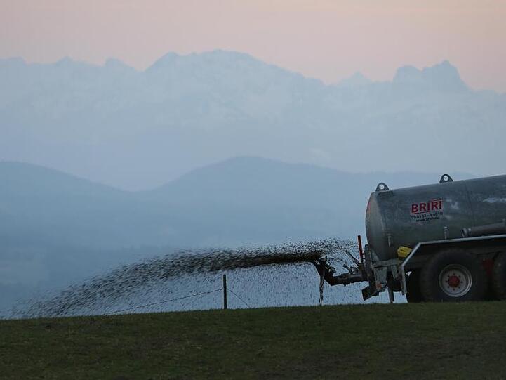 Ein Landwirt düngt auf dem 1055 Meter hohen Auerberg vor dem Panorama der Alpen eine Wiese mit Gülle.