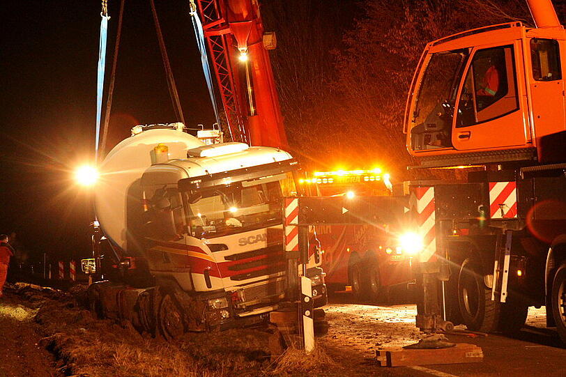 Ein Bergungsfahrzeug und zwei Kräne werden benötigt um den vollbeladenen LKW wieder auf die Straße zu ziehen.