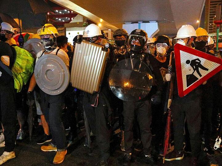 Demonstranten wappnen sich mit Straßenschildern, Koffern und Mülleimerdeckeln gegen die Schlagstöcke der Hongkonger Polizisten.