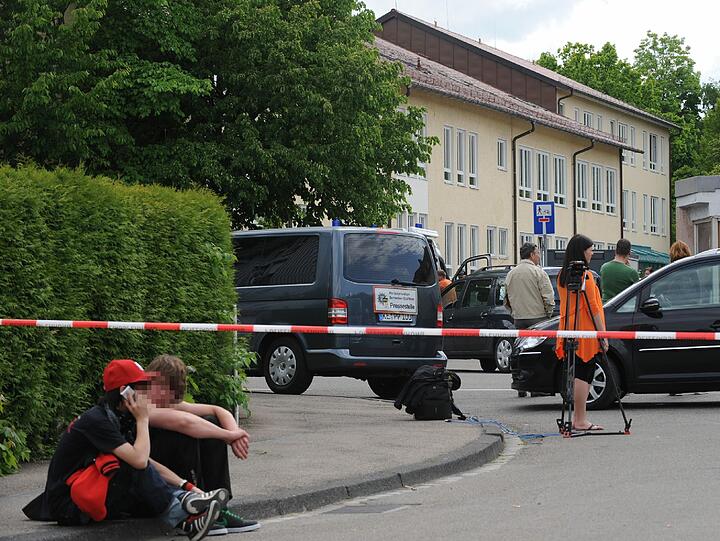 Zwei Jugendliche sitzen vor einem Absperrband an der Zufahrt zur Mittelschule in Memmingen, wo am Mittag Amok-Alarm ausgelöst wurde (Foto vom 22.05.12).