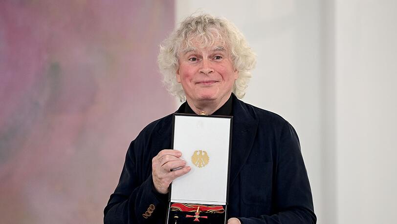 Sir Simon Rattle zeigt seine Auszeichnung.