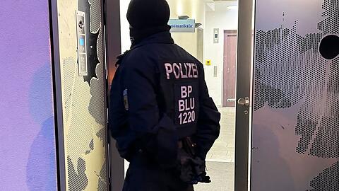 Ein Polizeibeamter steht bei einer Razzia in Berlin-Adlershof vor einem Gebäude.