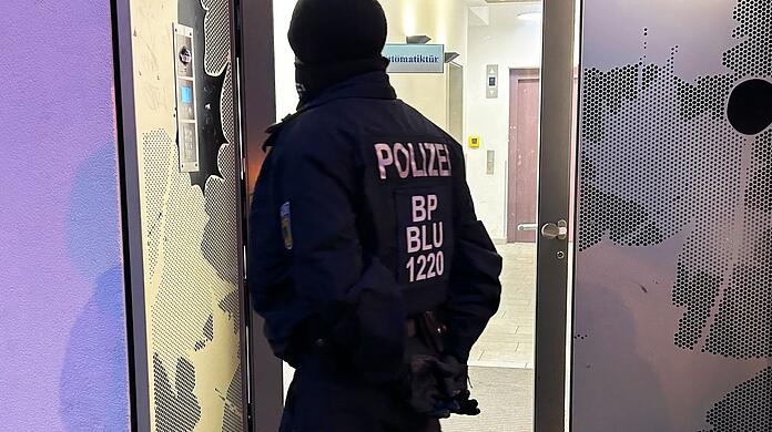 Ein Polizeibeamter steht bei einer Razzia in Berlin-Adlershof vor einem Gebäude.