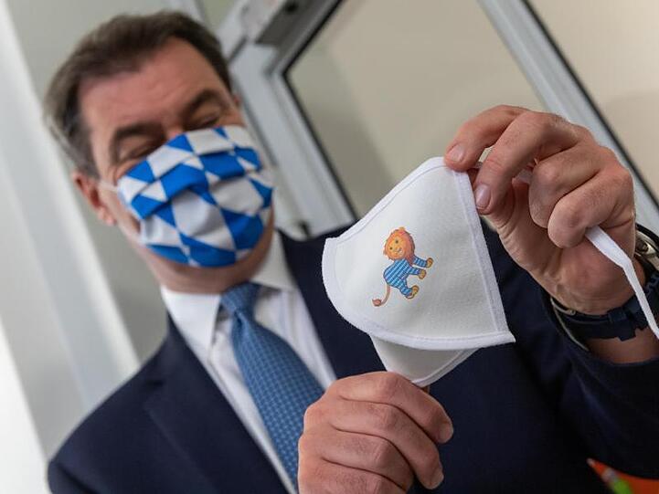 Markus Söder (CSU) präsentiert bei seinem Besuch einer Schule eine Mundschutzmaske für Schulkinder. Foto: Peter Kneffel/dpa