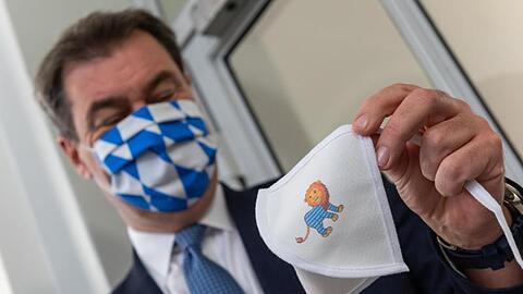 Markus Söder (CSU) präsentiert bei seinem Besuch einer Schule eine Mundschutzmaske für Schulkinder. Foto: Peter Kneffel/dpa
