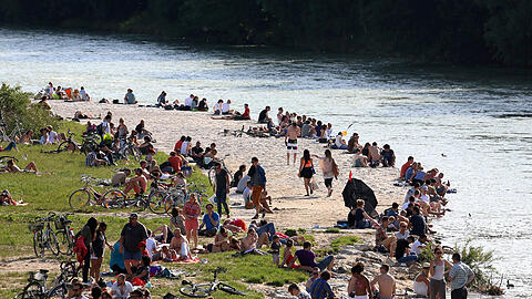 Menschen feiern bei schönem Wetter an der Isar.
