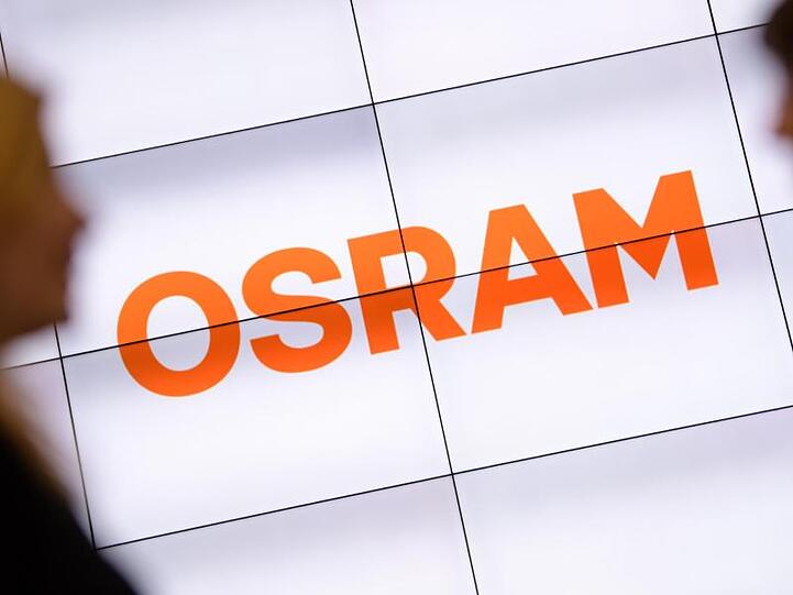 Zwei Frauen unterhalten sich vor einem über mehrere Monitore dargestellten Osram-Logo. Foto: Matthias Balk/Archivbild
