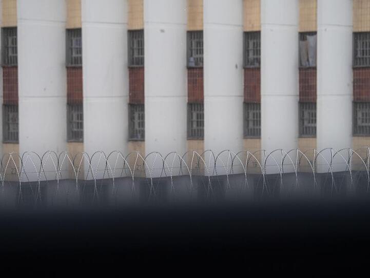 Stacheldraht liegt auf einer Gefängnismauer, im Hintergrund sind Zellenfenster der JVA Stuttgart-Stammheim zu sehen.