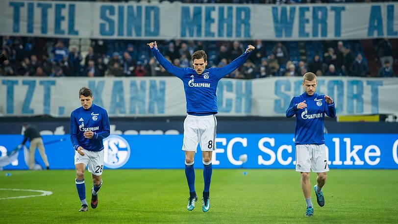 Leon Goretzka vor dem Spiel zwischen Schalke 04 und Hannover 96. Auf dem Plakat im Hintergrund steht: "Weder Kohle noch Titel sind mehr wert als unser Verein."