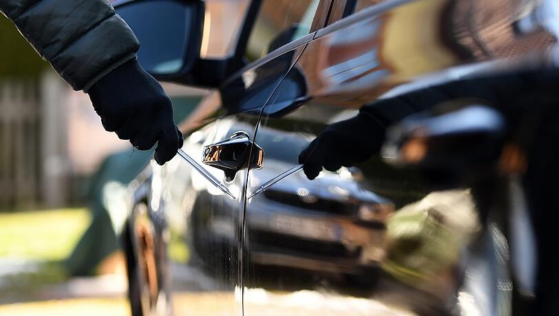 Ein Mann steht mit einem Schraubenzieher in seiner Hand gefährlich nahe neben einem Auto.