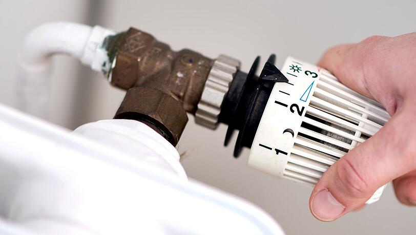 Eine Frau dreht am Thermostat eines Heizkörpers.