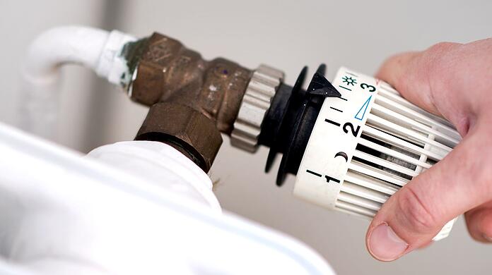 Eine Frau dreht am Thermostat eines Heizkörpers.