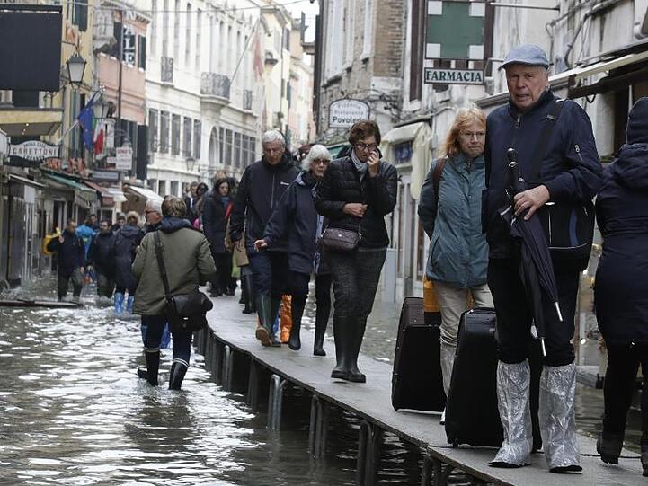 Touristen ziehen ihr Gepäck über provisorische Gehsteige.