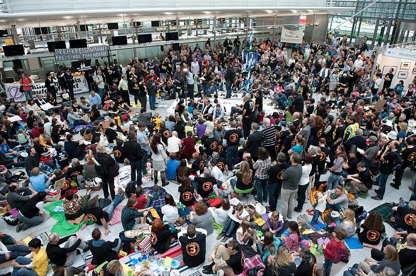 Demonstranten sitzen am Samstag (24.03.2012) am Terminal 2 des Münchner Flughafens auf Picknickdecken. Der Bund Naturschutz und das Aktionsbündnis AufgeMUCkt haben zum Protest-Picknick aufgerufen, um gegen den Bau einer dritten Startbahn am Münchner Flughafen zu demonstrieren.