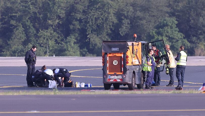 Sicherheitspersonal und Polizisten versuchen am Düsseldofer Flughafen, Aktivisten vom Asphalt auf dem Rollfeld zu lösen.