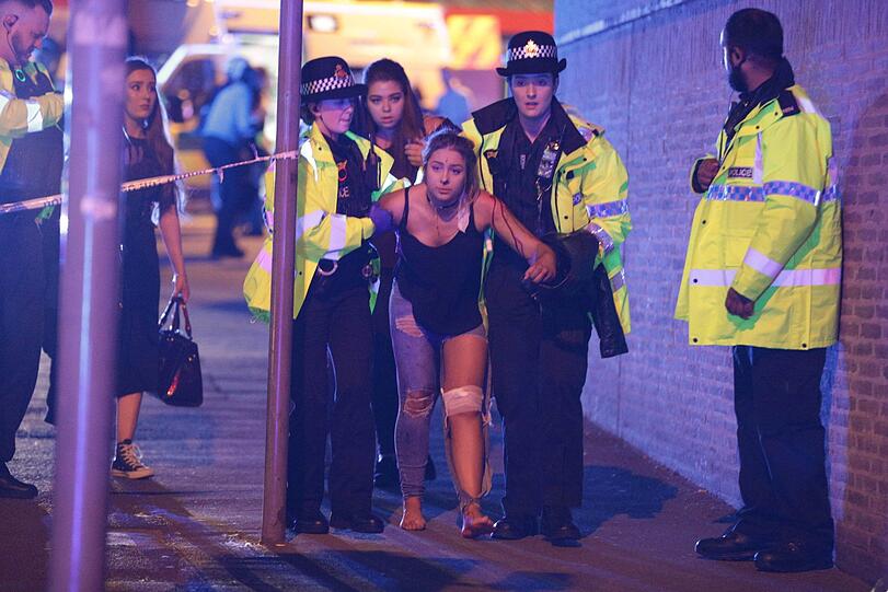 22.05.2017: Polizisten und andere Einsatzkräfte kümmern sich in Manchester (Großbritannien) in der Nähe der Manchester Arena um eine verletzte Frau. Bei einem Anschlag auf einem Konzert von Ariana Grande werden 23 Menschen getötet und 50 weitere verletzt.