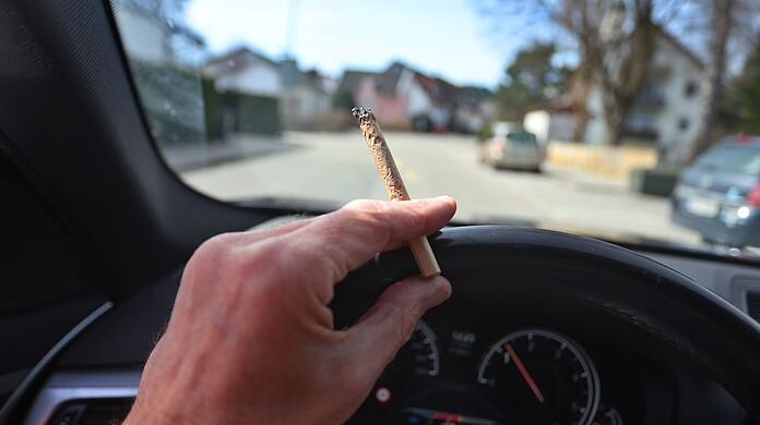 Eén man zit met één gewricht tussen de vingers aan het stuur en één auto.