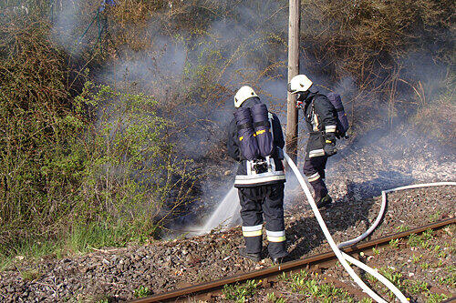 Feuerwehrmänner löschen einen Brand an einem Bahndamm.