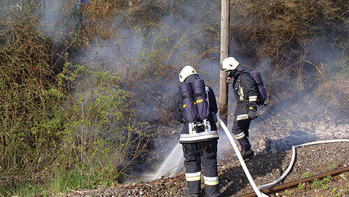Feuerwehrmänner löschen einen Brand an einem Bahndamm. Feuerwehrmänner löschen einen Brand an einem Bahndamm.