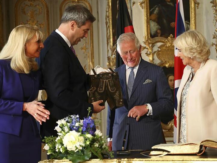 Markus Söder (CSU, 2.v.l) überreicht Prinz Charles und seiner Frau, Herzogin Camilla, eine Lederhose. Foto: Matthias Schrader/AP/Pool