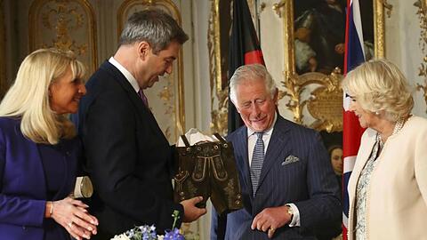 Markus Söder (CSU, 2.v.l) überreicht Prinz Charles und seiner Frau, Herzogin Camilla, eine Lederhose. Foto: Matthias Schrader/AP/Pool