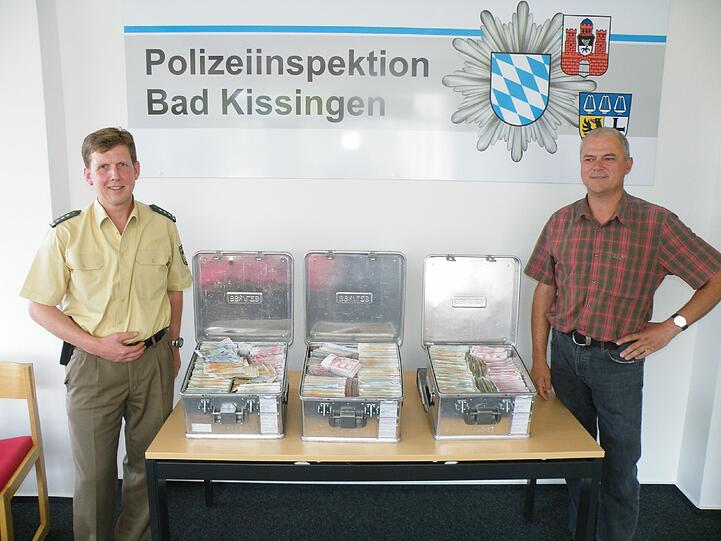 Polizeihauptkommissar Stefan Haschke (l.), Leiter der Polizeiinspektion Bad Kissingen, und Sachbearbeiter der Kripo Schweinfurt, Kriminalhauptkommissar Thomas Brandl neben den drei gefuellten Geldkoffern.