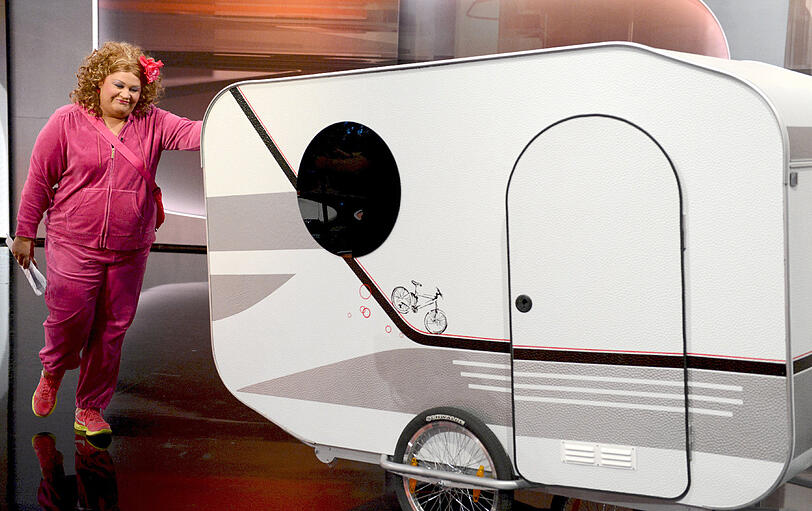 Und natürlich ist das Ganze geplant: Aus dem kleinen Wohnwagen steigt die füllige Comedian Cindy aus Marzahn.