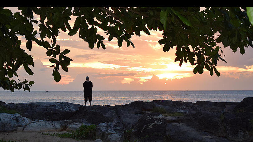 Eine Frau blickt am Strand vor Khao Lak in den Sonnenuntergang. Hier...