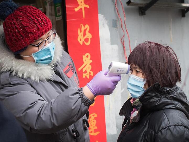 Eine Gemeindemitarbeiterin misst die Körpertemperatur einer Passantin in der Nähe der Kranichpagode in Wuhan.