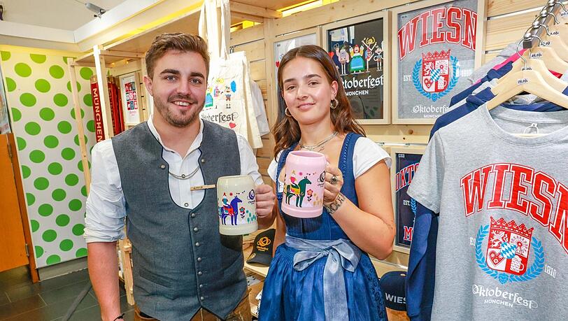 Neben dem offiziellen Oktoberfest-Jahresmaßkrug 2024 gibt es noch andere lizenzierte Krüge. Zum Beispiel dieses Duo aus einem steingrauen und einem rosa Keramik-Bierkrug (0,5 Liter) - hier präsentiert von Lorenz Krüger und Anneke Jenter aus dem Oktoberfest-Pop-up-Laden am Marienplatz.