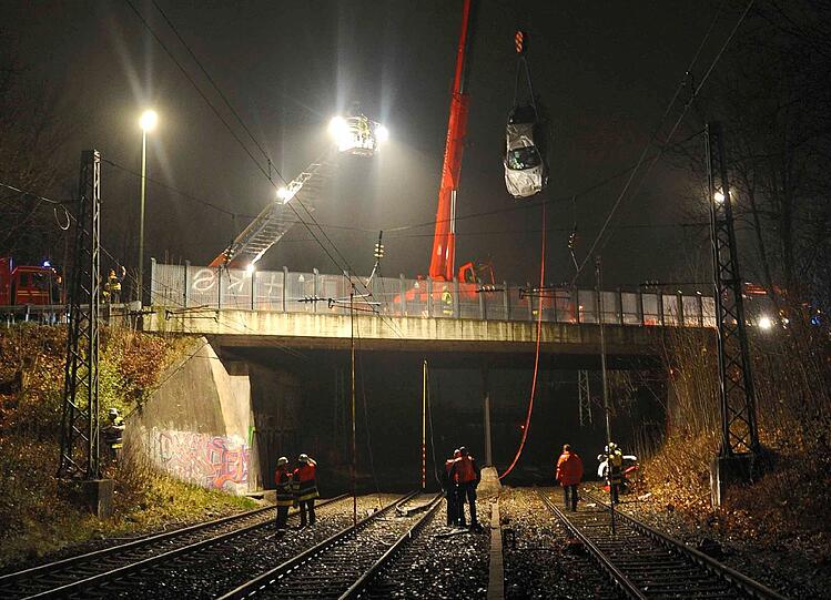 Ganz oben rechts hängt das Wrack am Haken. Die Feuerwehr kümmert sich um den Unfallort