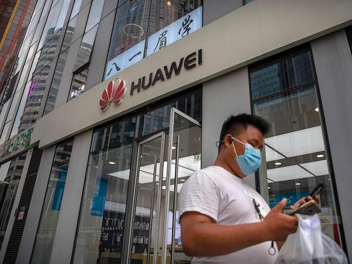 Ein Mann mit Gesichtsmaske schaut auf sein Smartphone, als er an einem Huawei-Laden in Peking vorbeigeht.