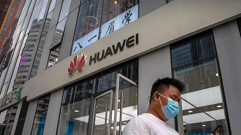 Ein Mann mit Gesichtsmaske schaut auf sein Smartphone, als er an einem Huawei-Laden in Peking vorbeigeht.