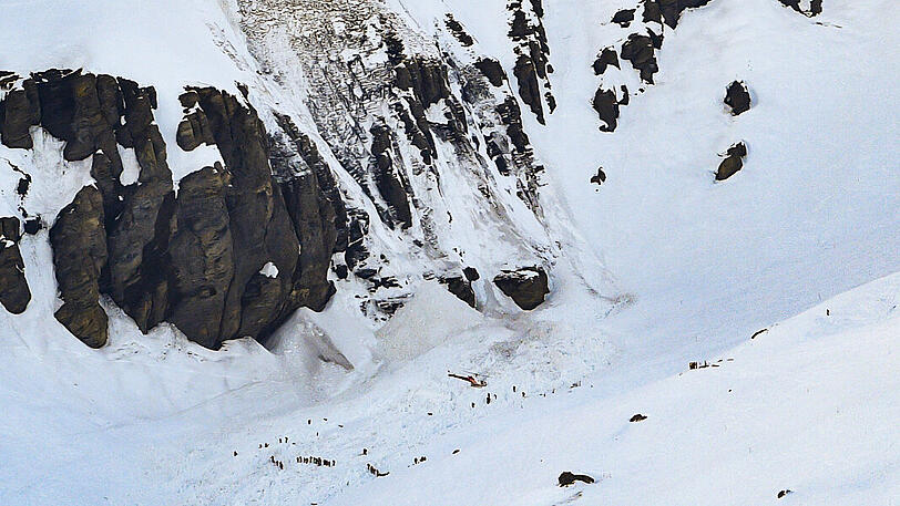 Ein Rettungshubschrauber fliegt über Rettungskräften, die in einem Lawinengebiet im Skigebiet Crans Montana im Einsatz sind.