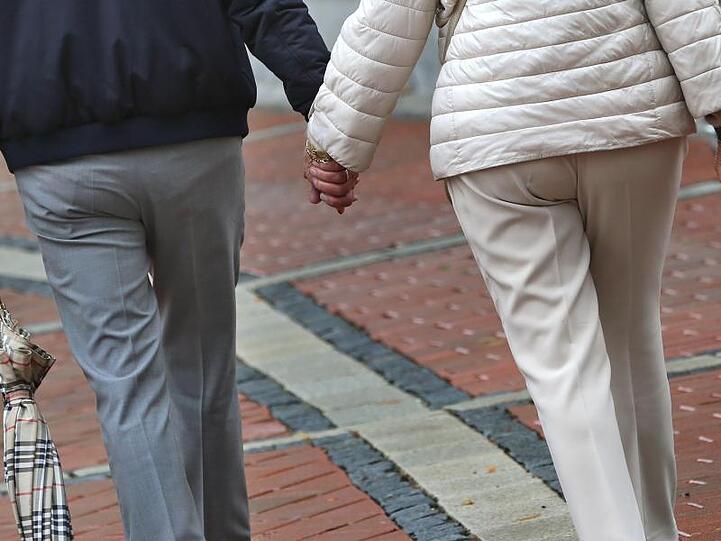 Ein älteres Paar Hand in Hand in einer Fußgängerzone.