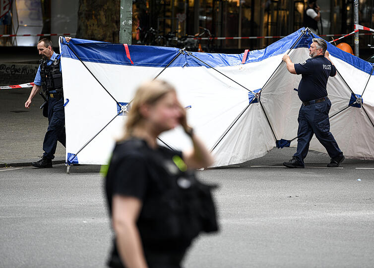 Einsatzkräfte tragen nach dem Zwischenfall auf der abgesperrten Straße einen Sichtschutz.