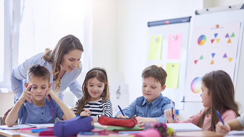 Eine Lehrerin hilft Kindern bei den Aufgaben. Die Landtags-SPD beklagt zu viele ausgefallene Unterrichtsstunden und Lehrermangel.